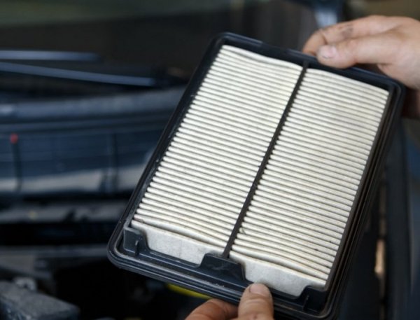 une personne tenant un filtre à air devant une voiture