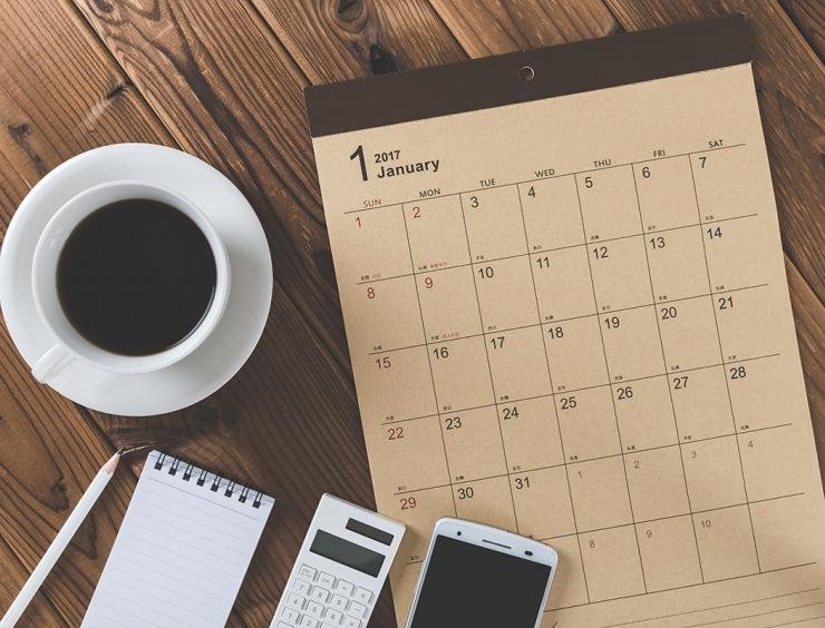 un bureau avec un calendrier, un téléphone portable et une tasse de café