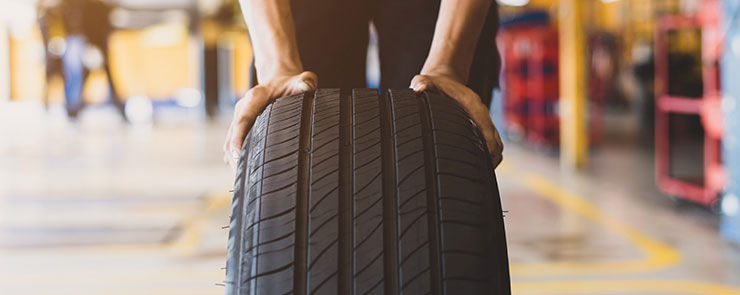A handsome young mechanic in white gloved uniform is putting his hand on a new tire and checking and checking the condition of the tire while doing car service.