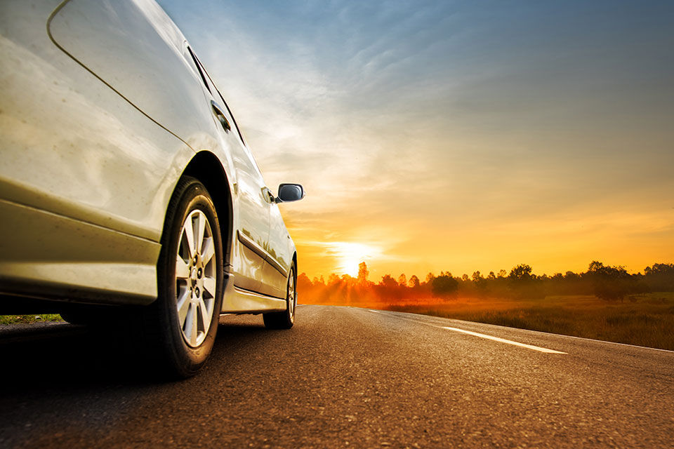 une voiture blanche roulant sur une route au coucher du soleil